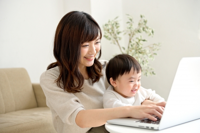 子どものそばでパソコンを使って在宅ワークをする女性